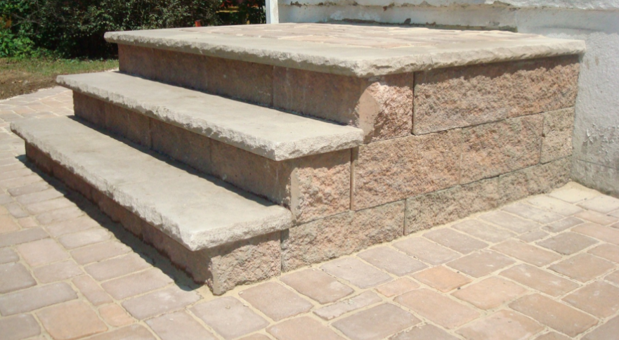 Stone steps leading up to a building entrance.  The steps have a textured appearance and are bordered by brick pavers.