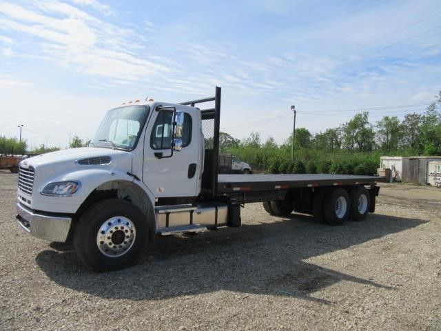 White flatbed tow truck parked on gravel under a blue sky