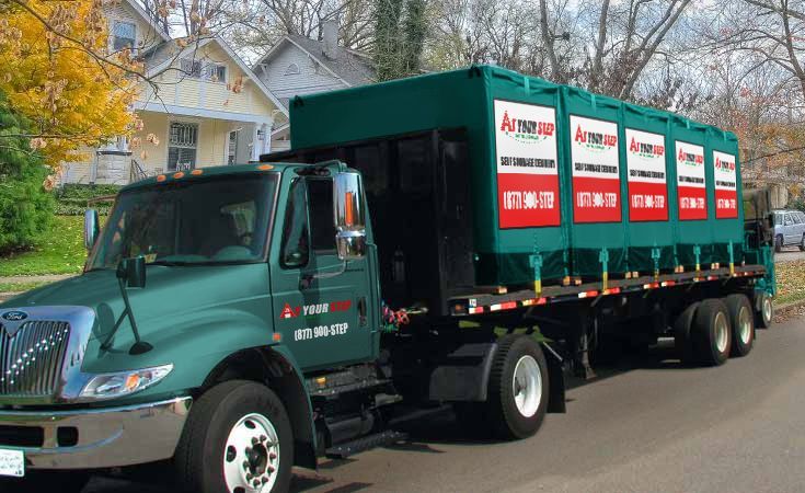 Green dump truck hauling a covered load on a residential street in autumn