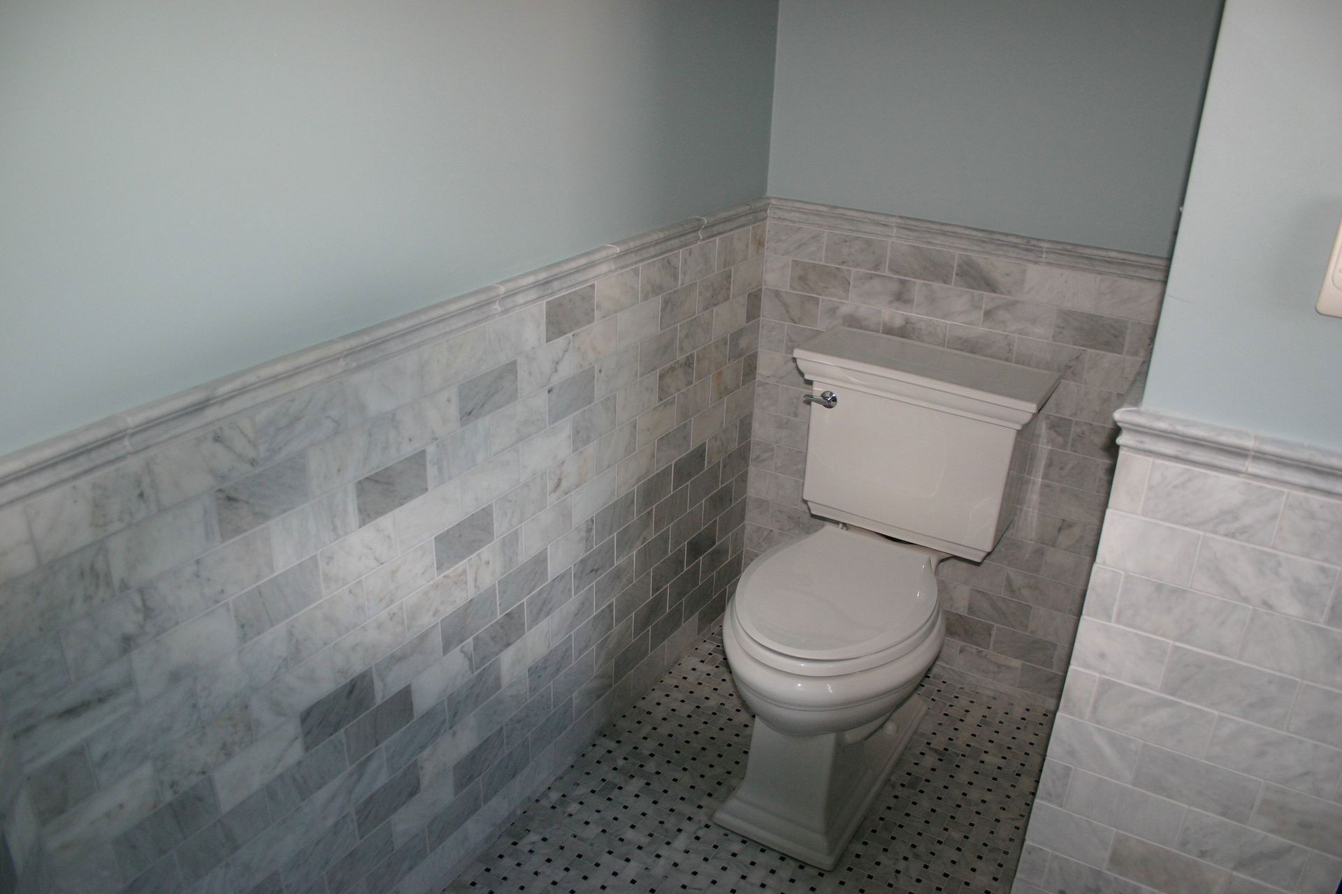 Small tiled bathroom with a white toilet and light gray walls.