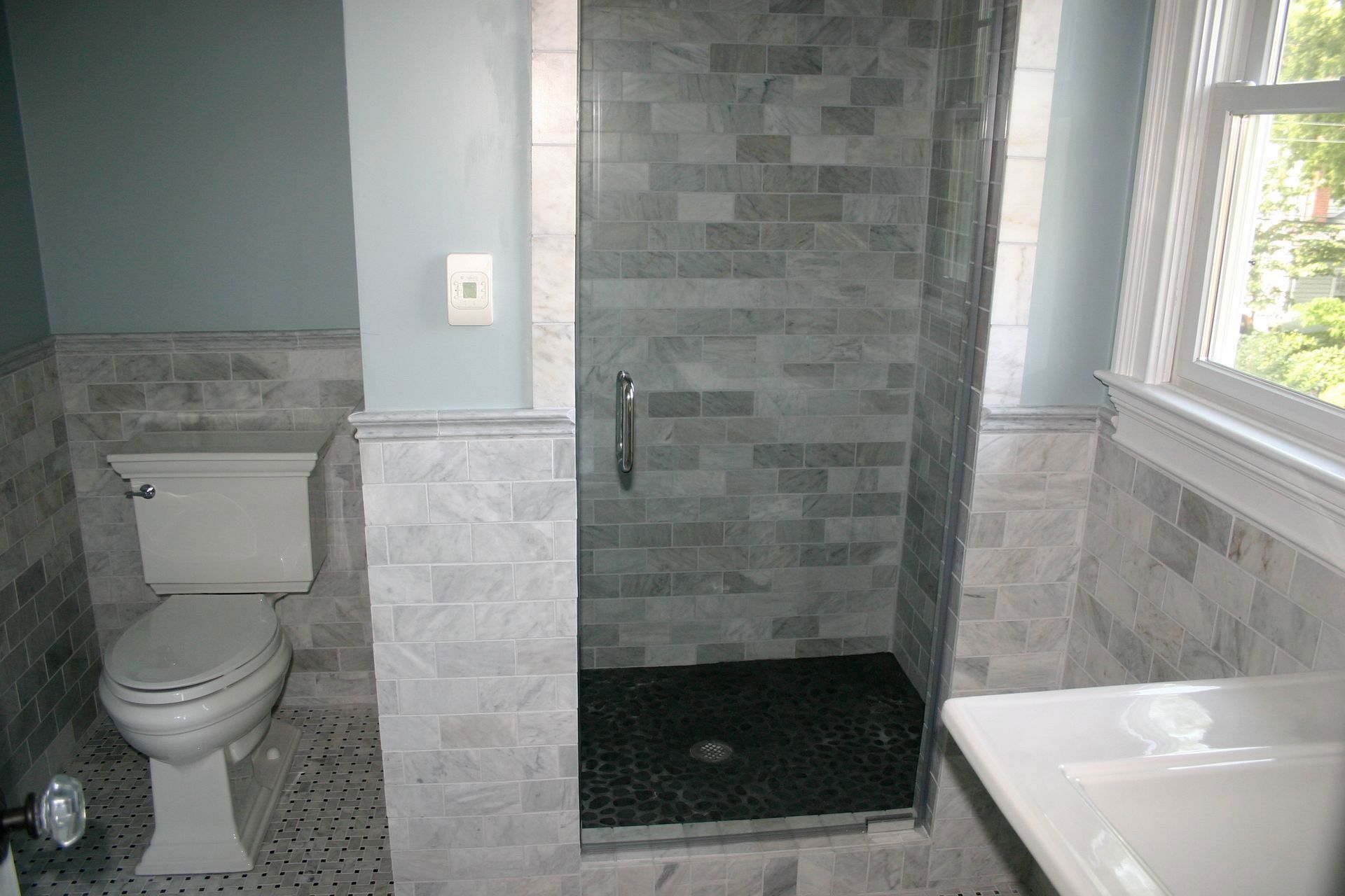 Bathroom with tiled shower, toilet, and sink by a window and frosted glass door.