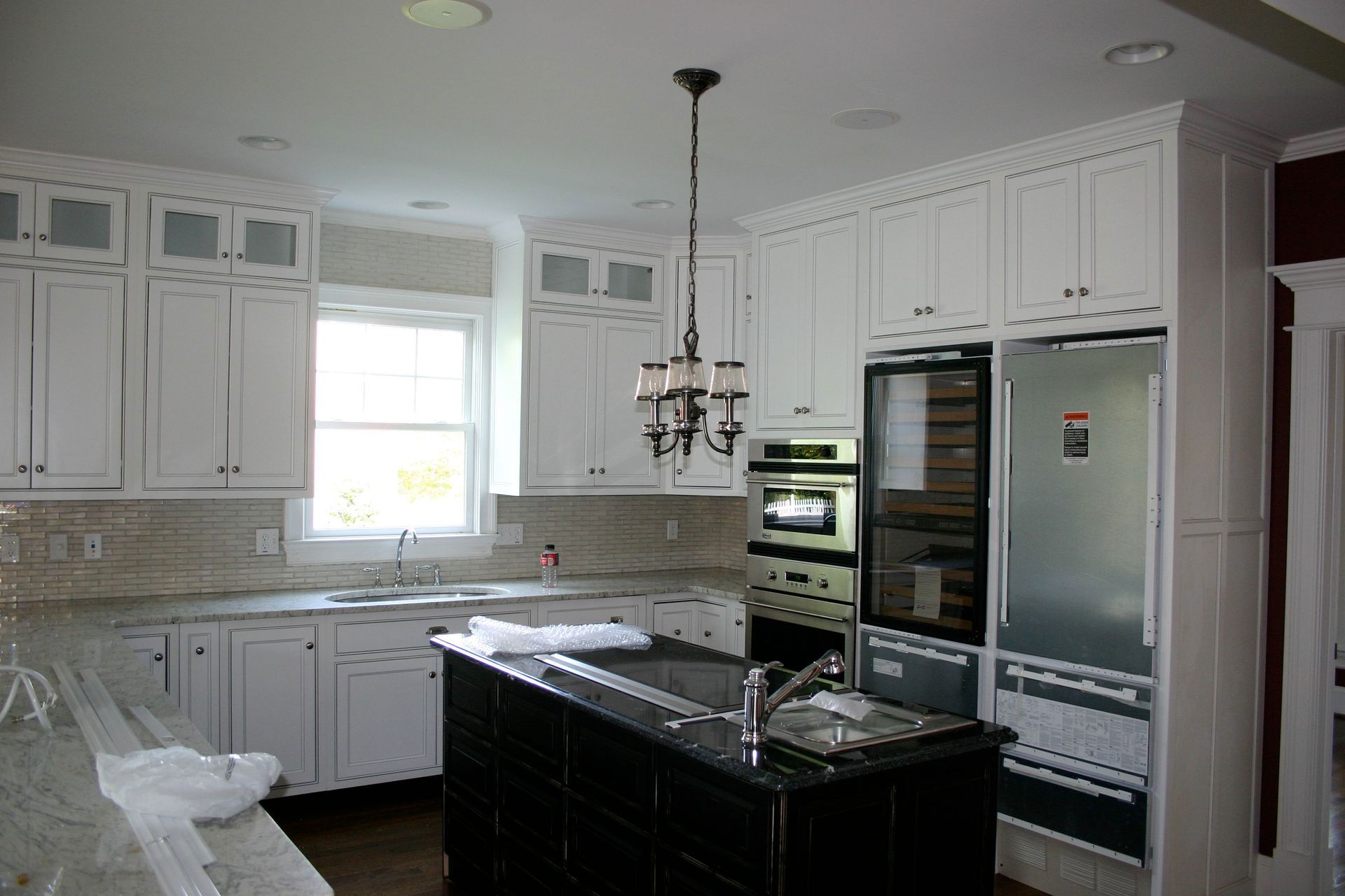 Bright white kitchen with granite island, stainless appliances, and a hanging light fixture