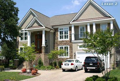Tan and stone-clad house with cars in the driveway, blue sky.