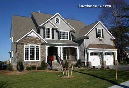 Gray, multi-story house with stone and shingle siding, two-car garage, and green lawn.