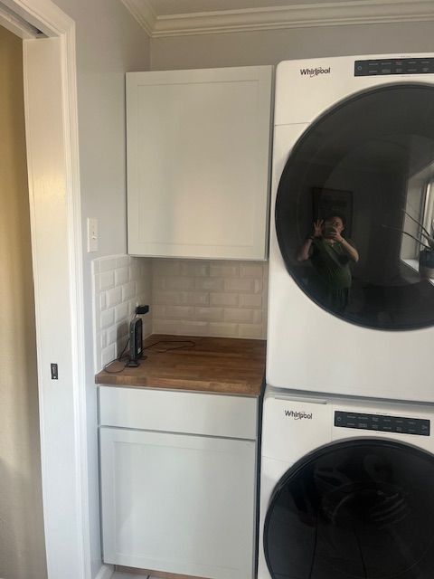 Laundry room with stacked white Whirlpool washer and dryer, cabinetry, and wooden countertop.