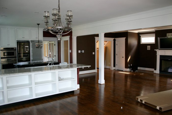 Open-concept kitchen and living room with white cabinetry, brown walls, hardwood floors, and a large chandelier.
