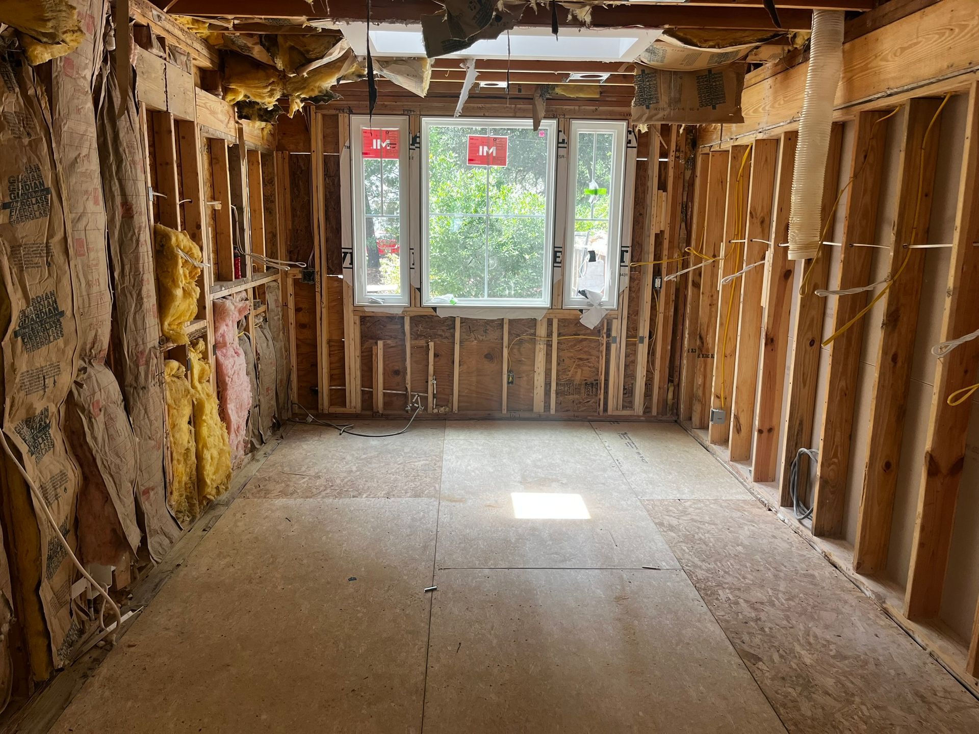 Interior room under construction, with exposed wooden studs, insulation, and a window.