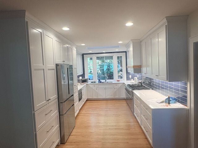 A newly renovated kitchen with white cabinets, stainless steel appliances, and wood flooring.