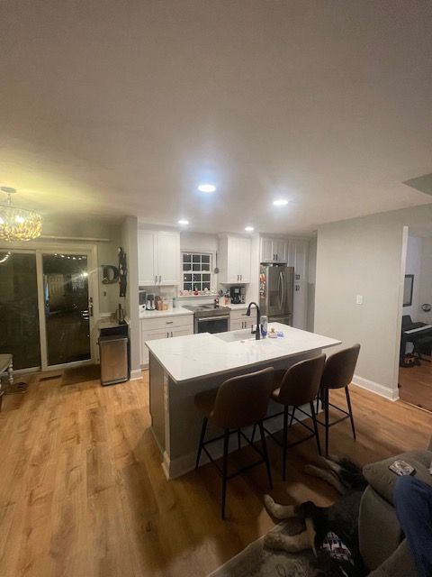Modern kitchen with white cabinets, island, wooden floor, and bar stools.