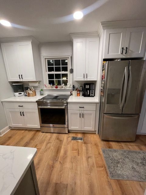 White kitchen cabinets with black hardware, stainless steel appliances, and wood-look flooring.
