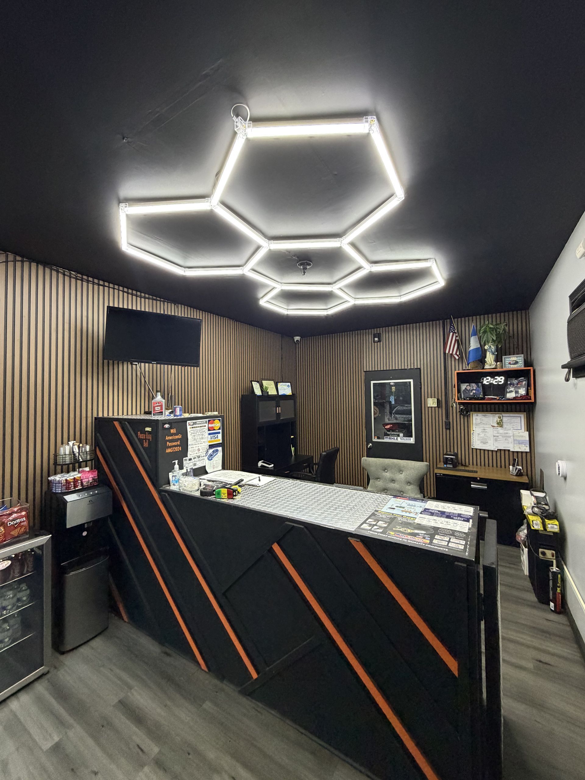 Modern reception desk in a small office with hexagonal ceiling lights and wood-paneled walls.