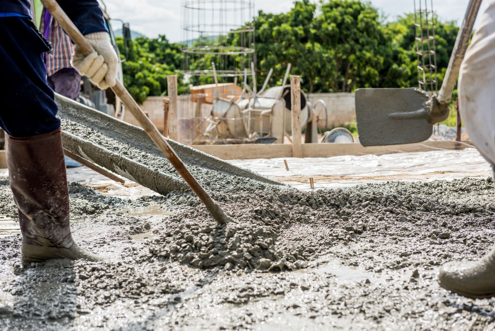 Construction workers leveling wet cement with shovels and wooden tools. Outdoor setting, day.