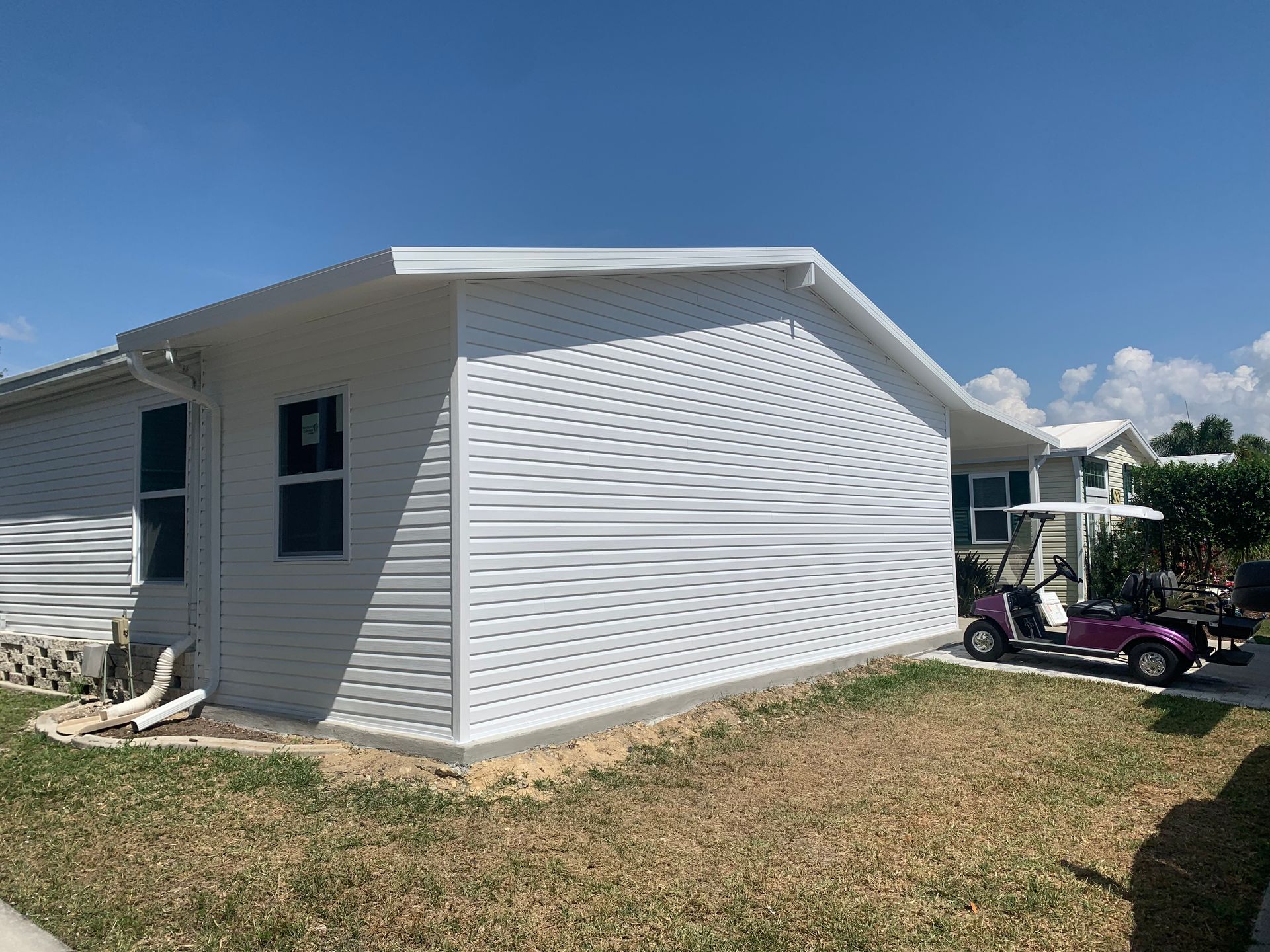 White vinyl house exterior with blue trim on a sunny day, shown from the side with a lawn in front