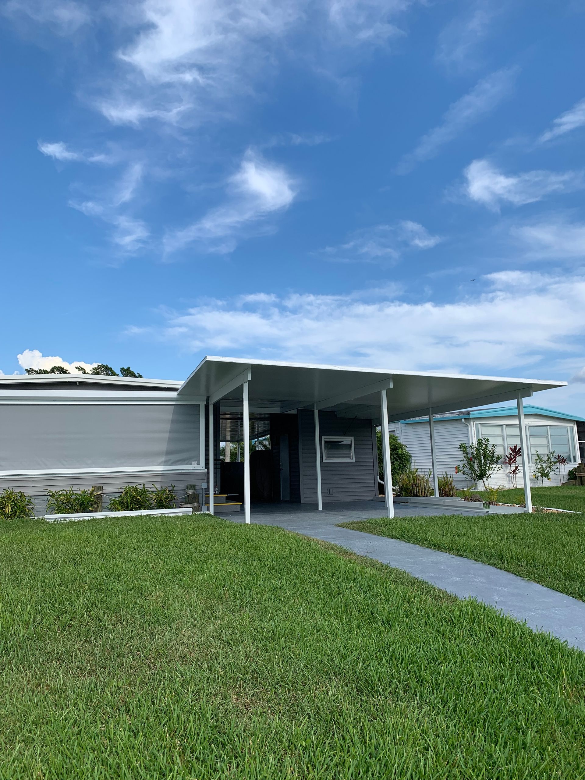 Low white building with a covered entrance, green lawn, and blue sky with clouds.