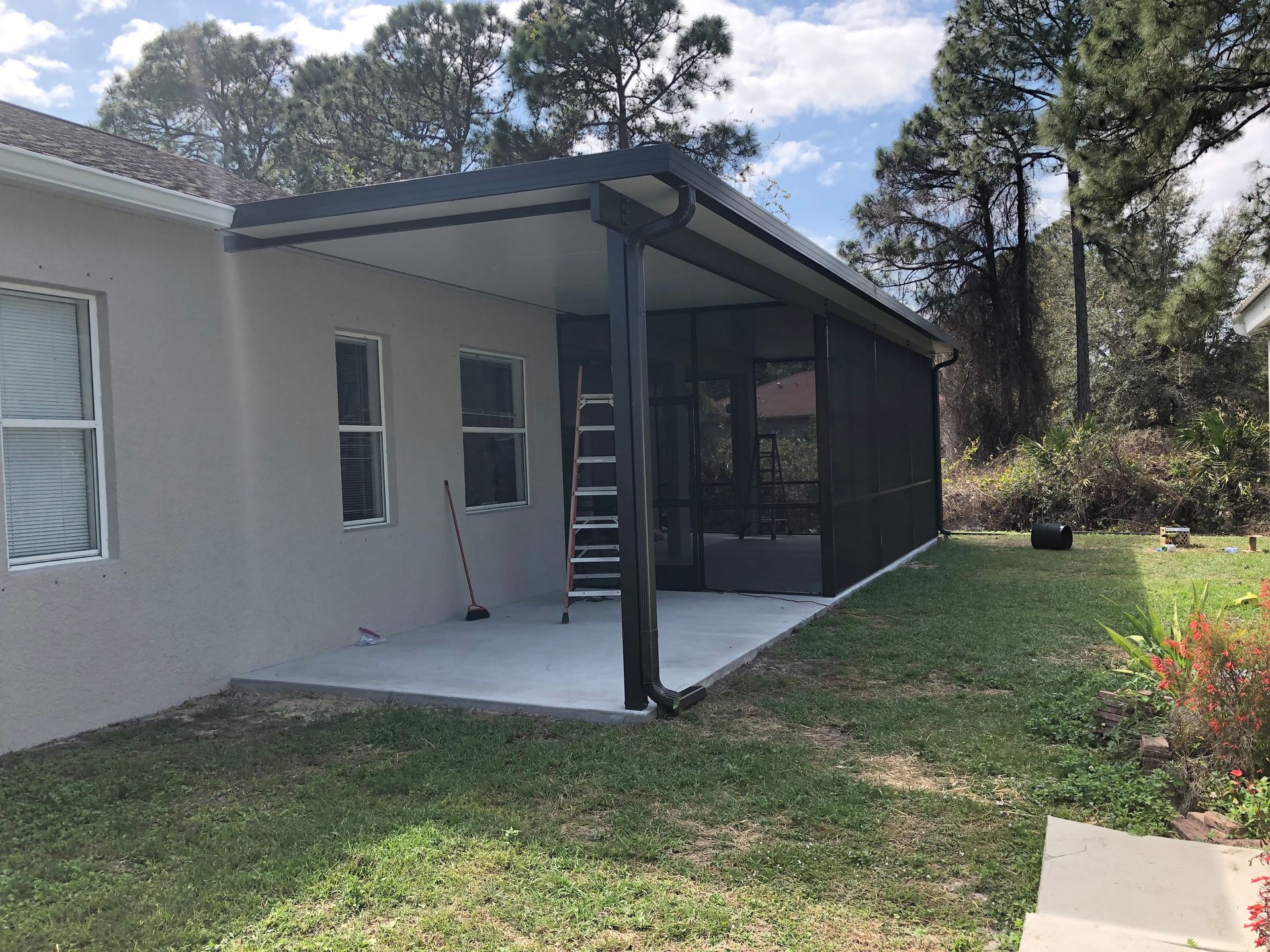 Back patio with screened porch, black supports, and concrete slab beside a house and lawn.