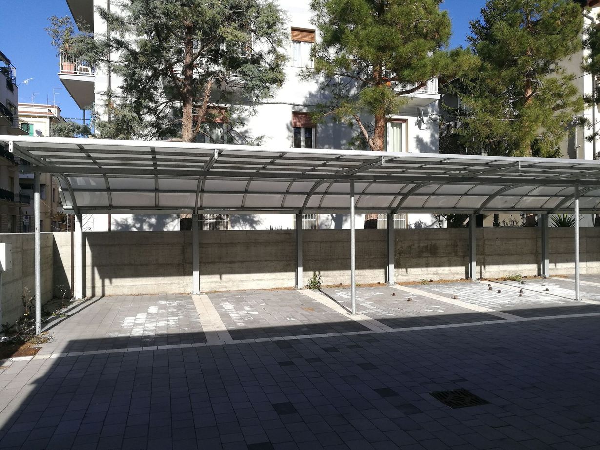 Covered parking area with empty concrete spaces and trees behind it