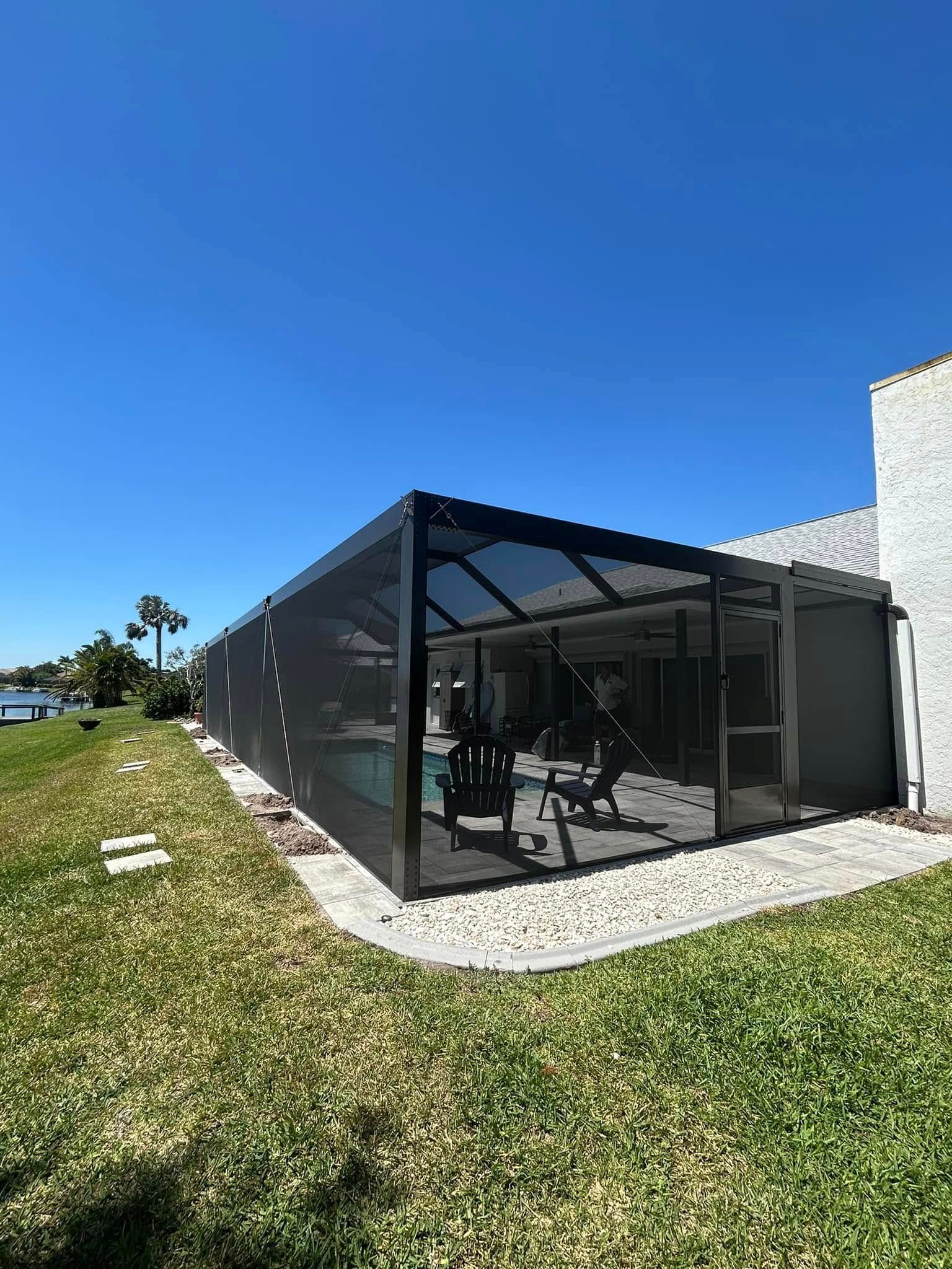 Outdoor screened patio with black frame and glass doors beside a white building under a clear blue sky