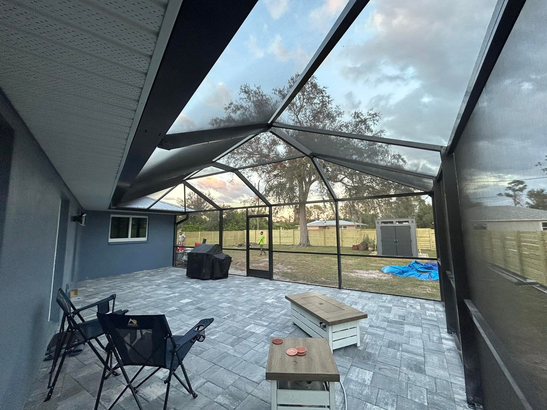 Covered patio with black screened enclosure, gray pavers, patio chairs, and a backyard view.