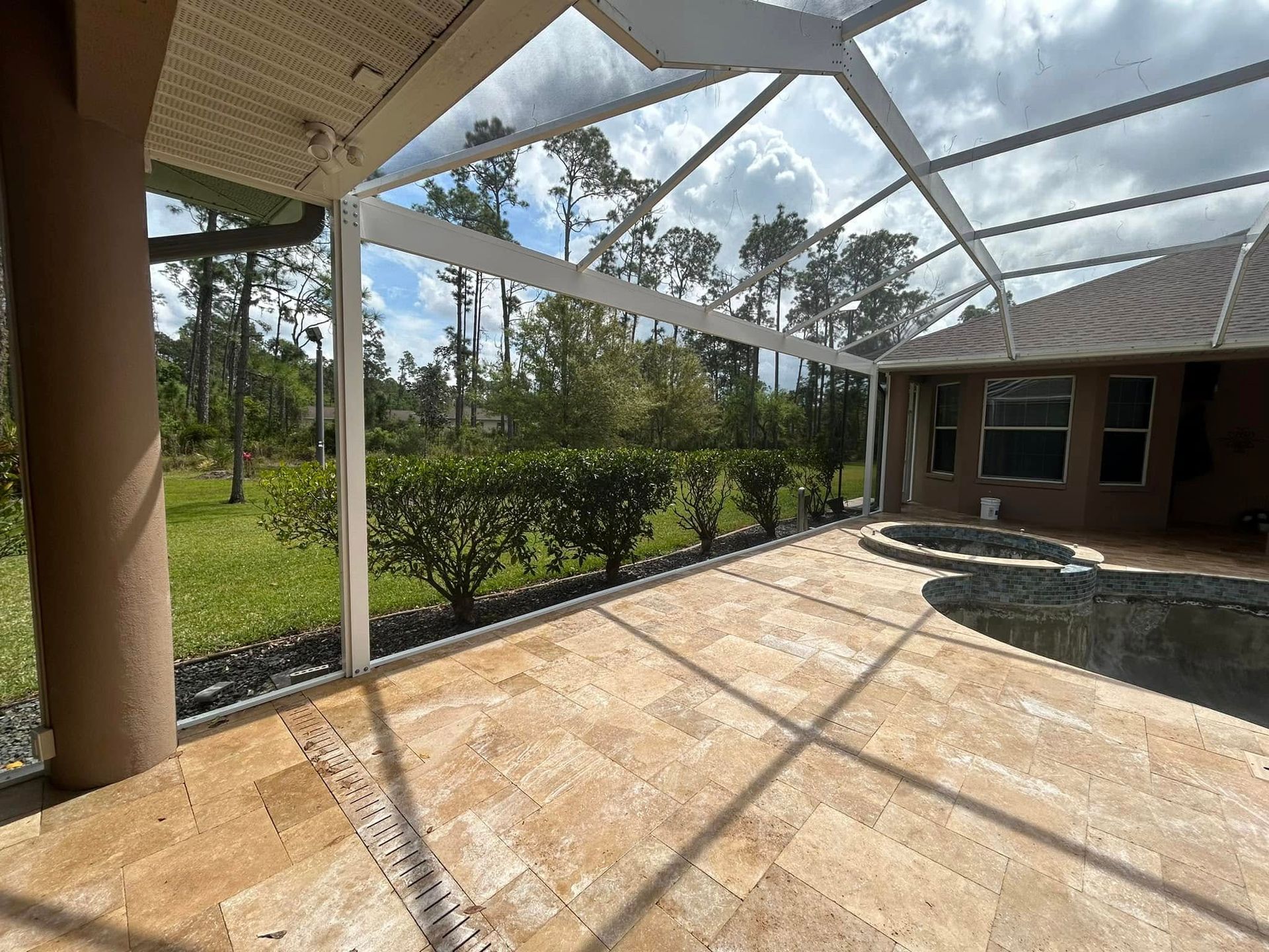 Screened patio with tiled floor, screened roof, and view of grassy yard and trees beyond.