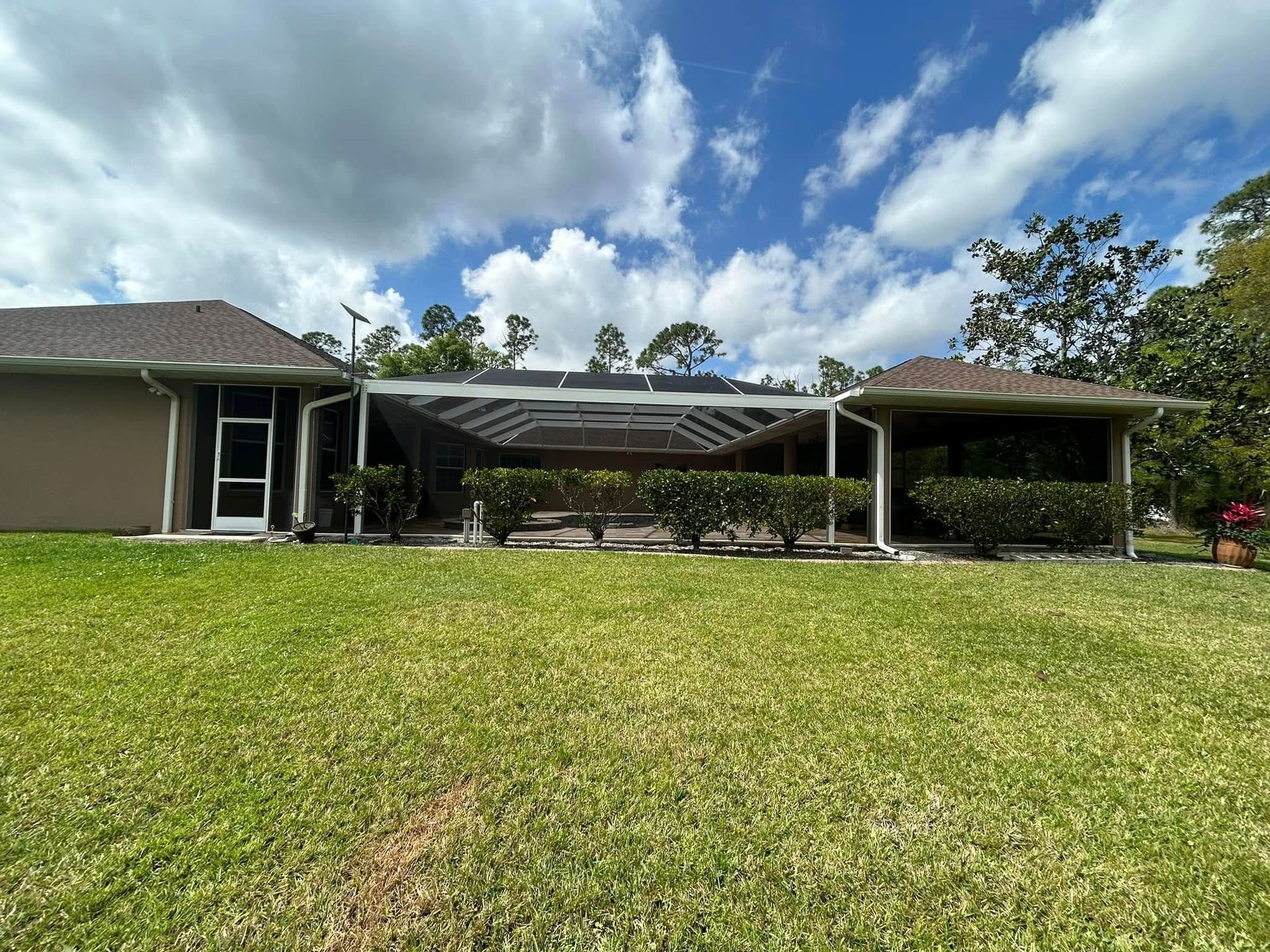 Single-story house with a large green lawn, covered patio, and partly cloudy blue sky