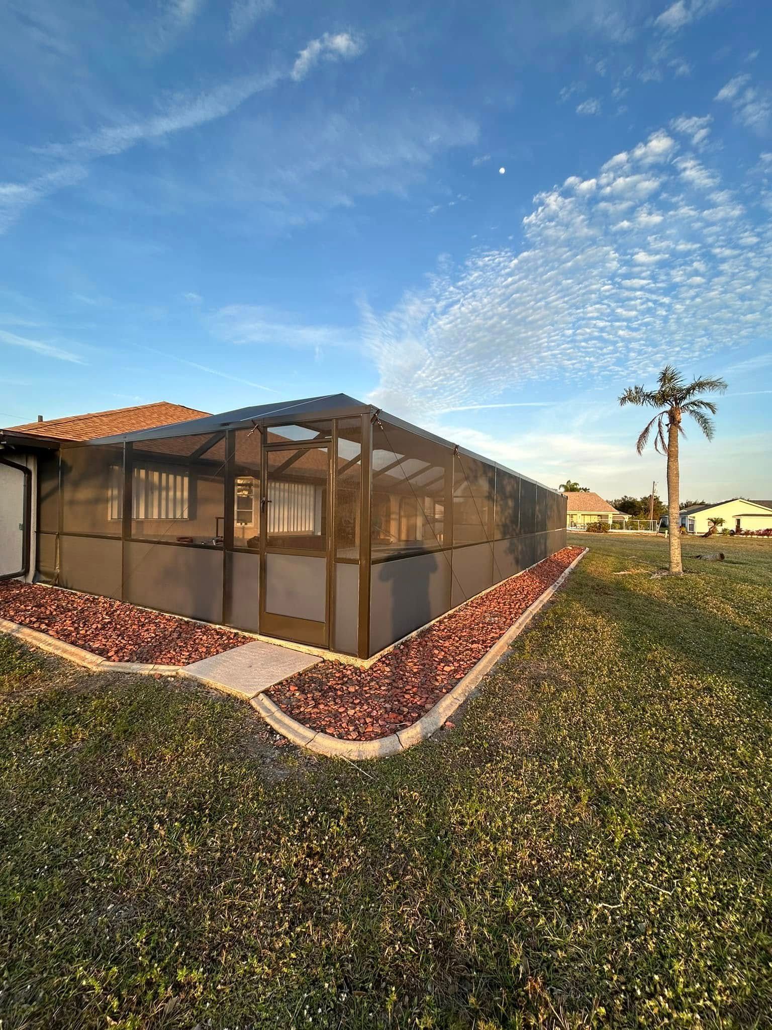 Screened patio beside a house with red tile roof, landscaped yard, and a palm tree under a blue sky.