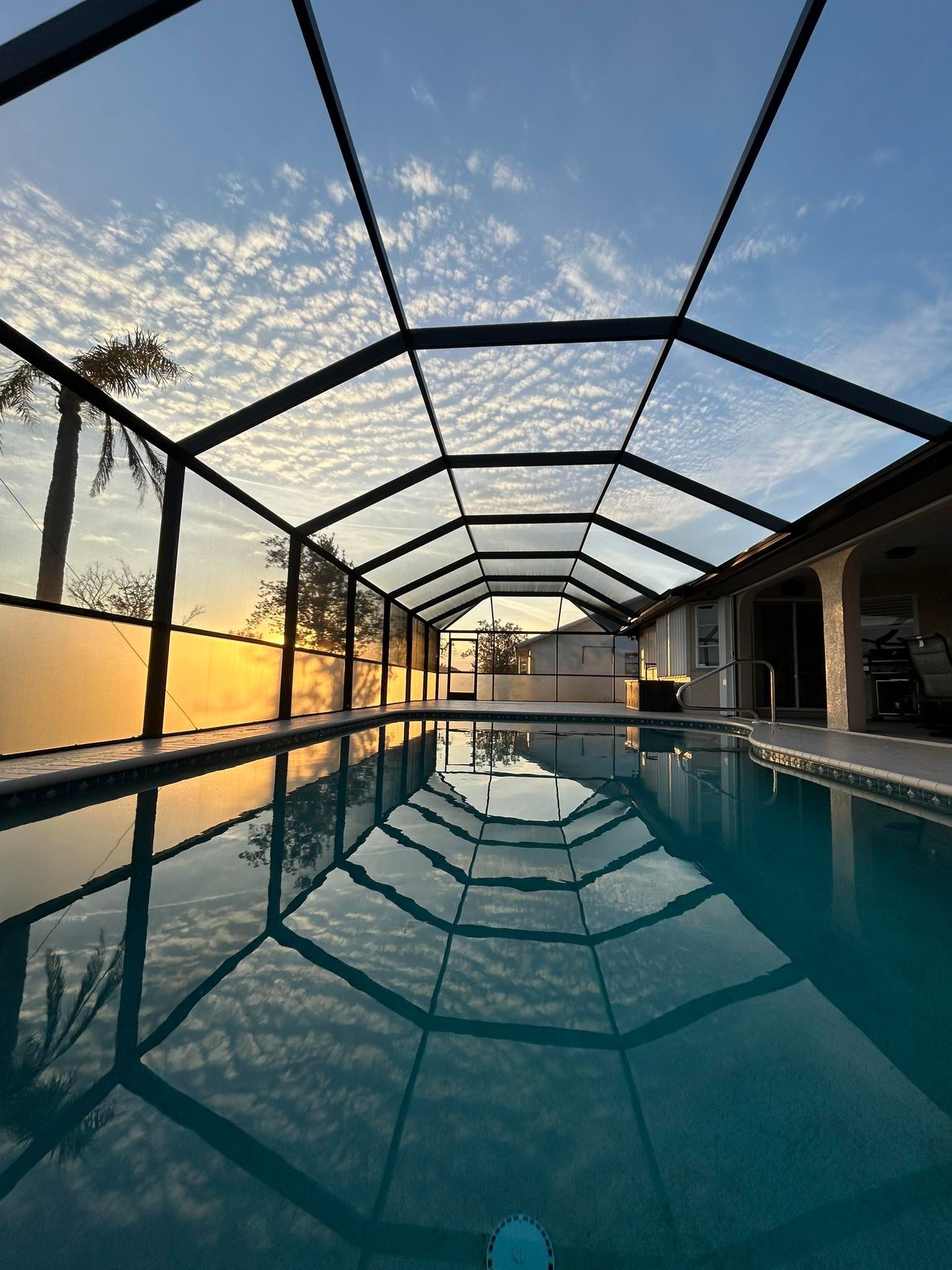 Indoor swimming pool at sunset with a screened enclosure and calm water reflecting the structure