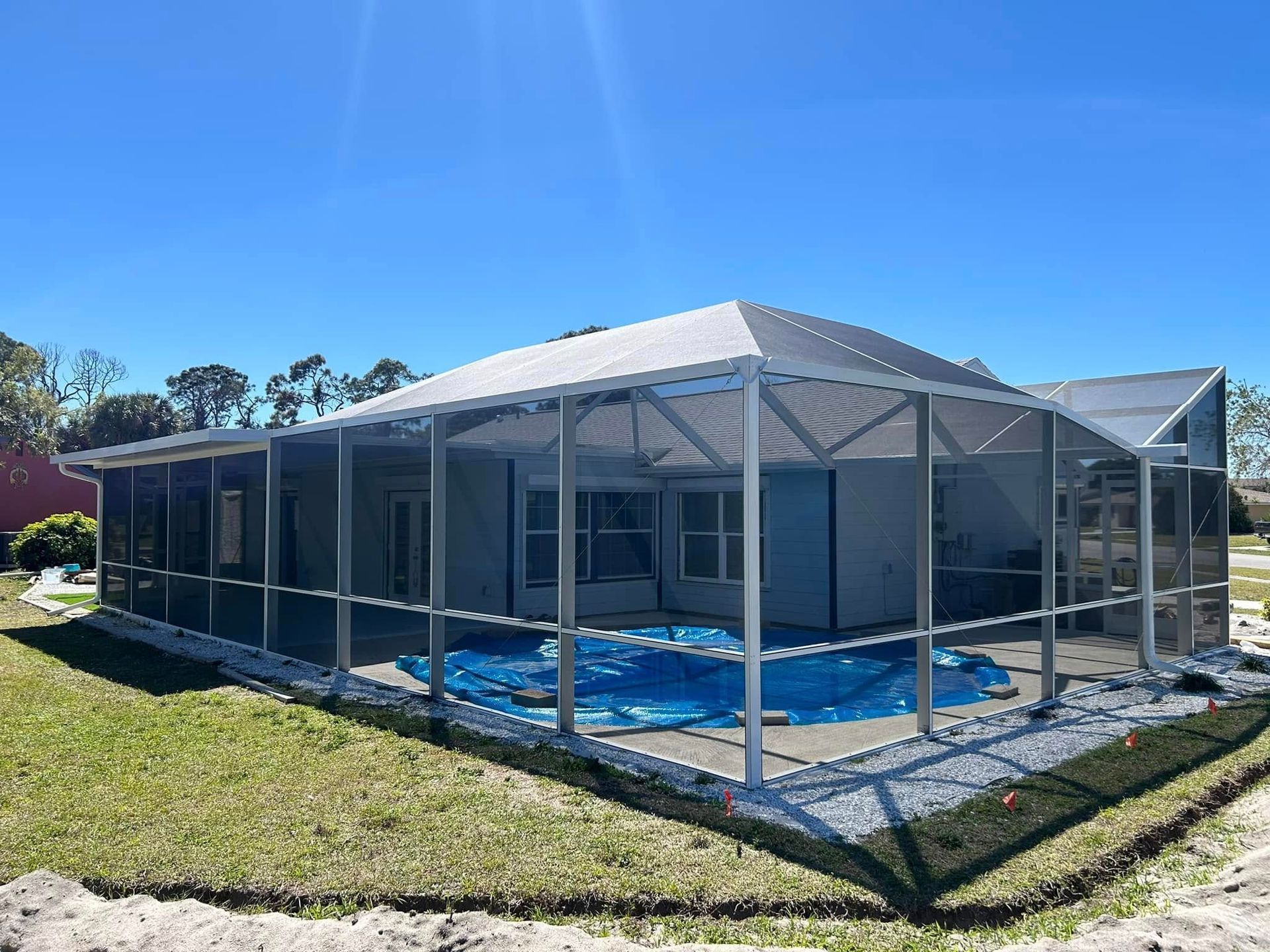 Screened patio beside a house with a white canopy and blue flooring under a clear sky