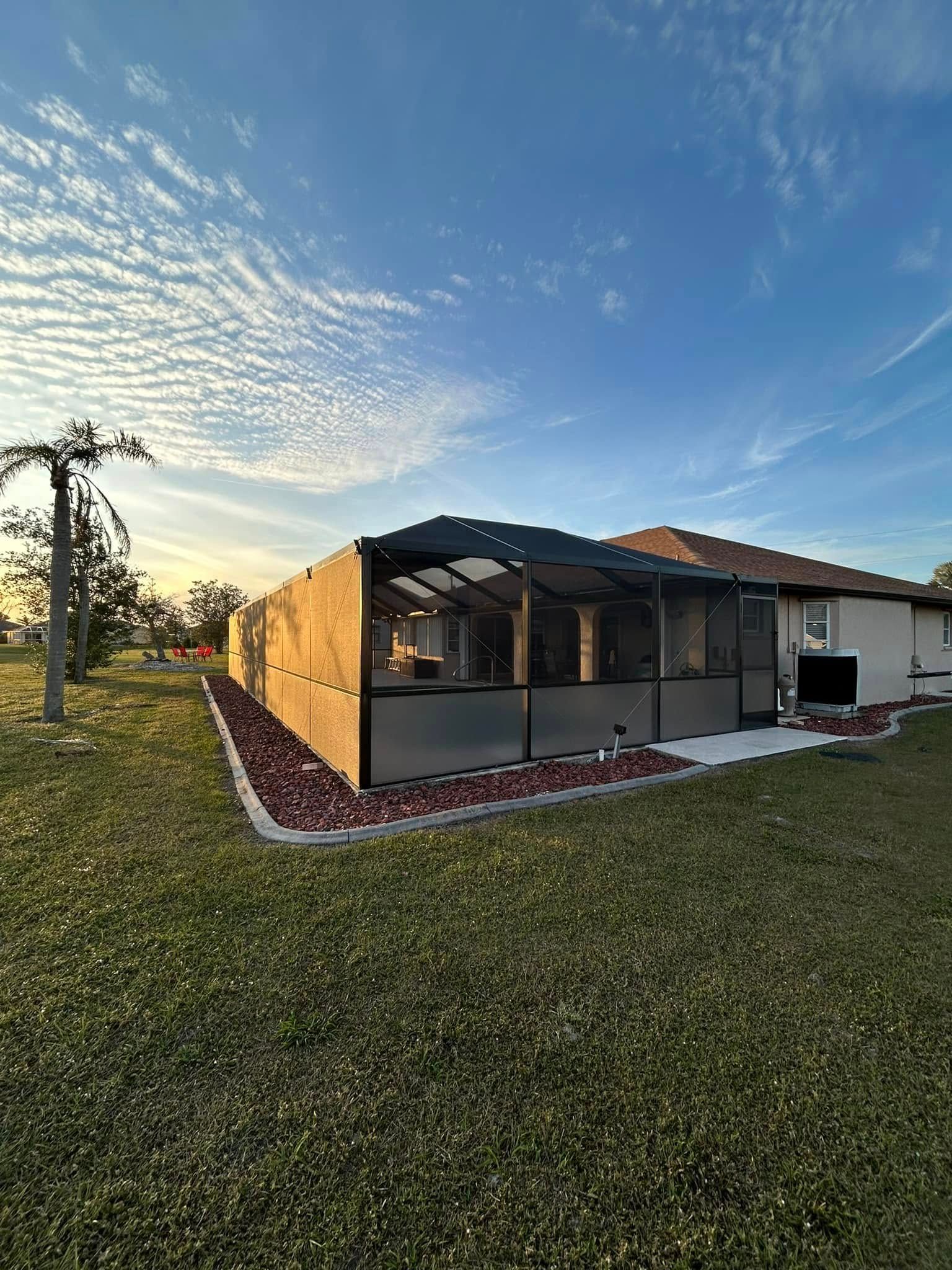 Backyard screened patio addition beside a house at sunset, with a grassy lawn and flowering border