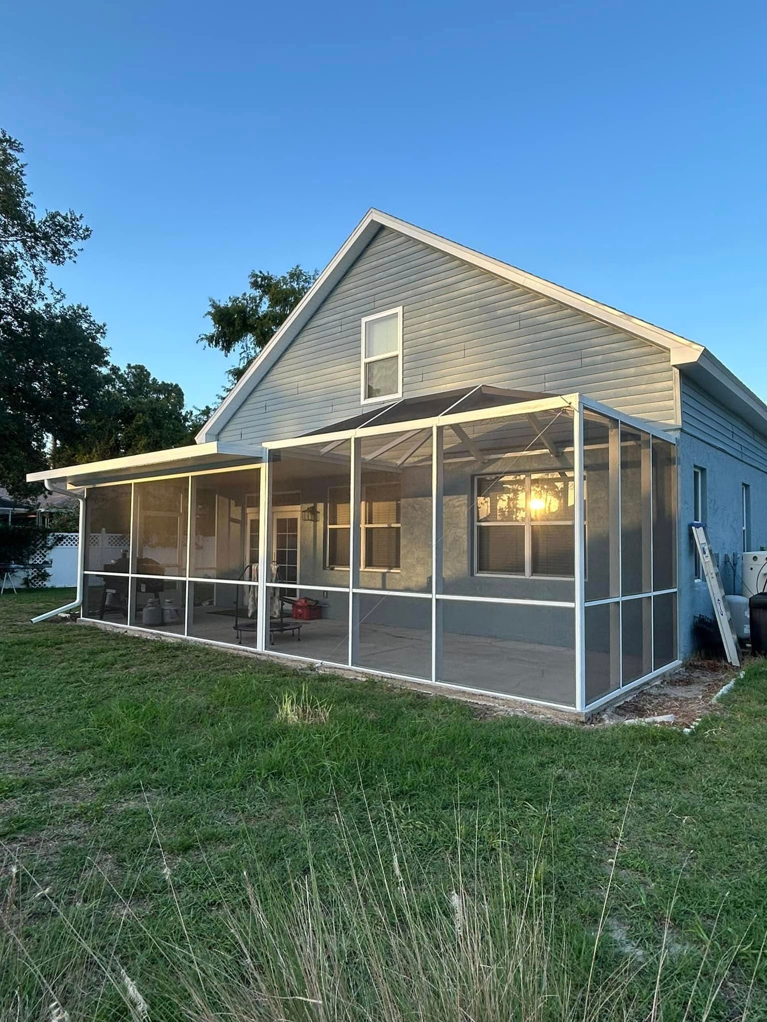 Small gray house with a screened porch, lit windows, and a grassy yard at dusk