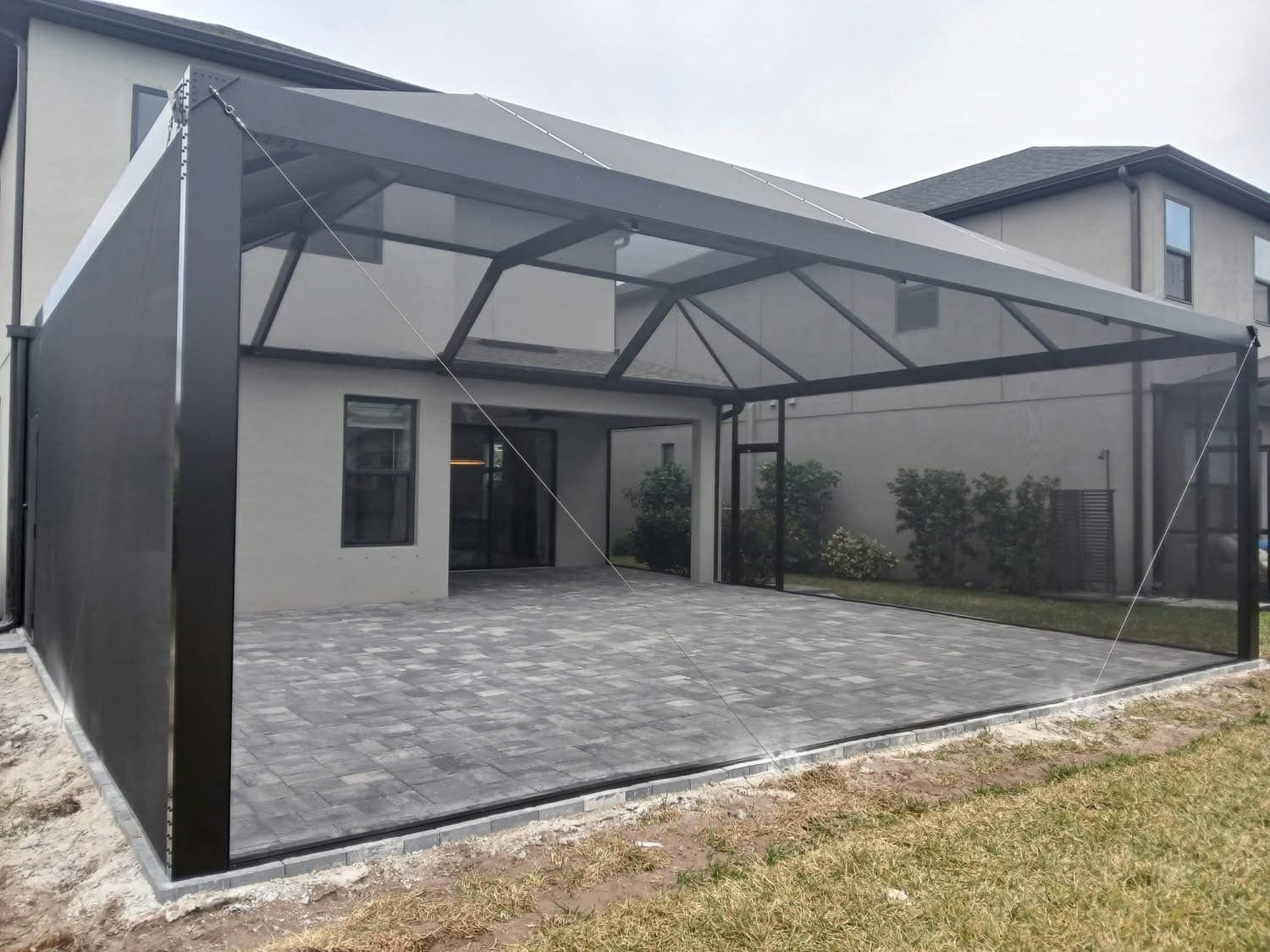 Covered outdoor patio with black metal frame and gray paver floor beside a house