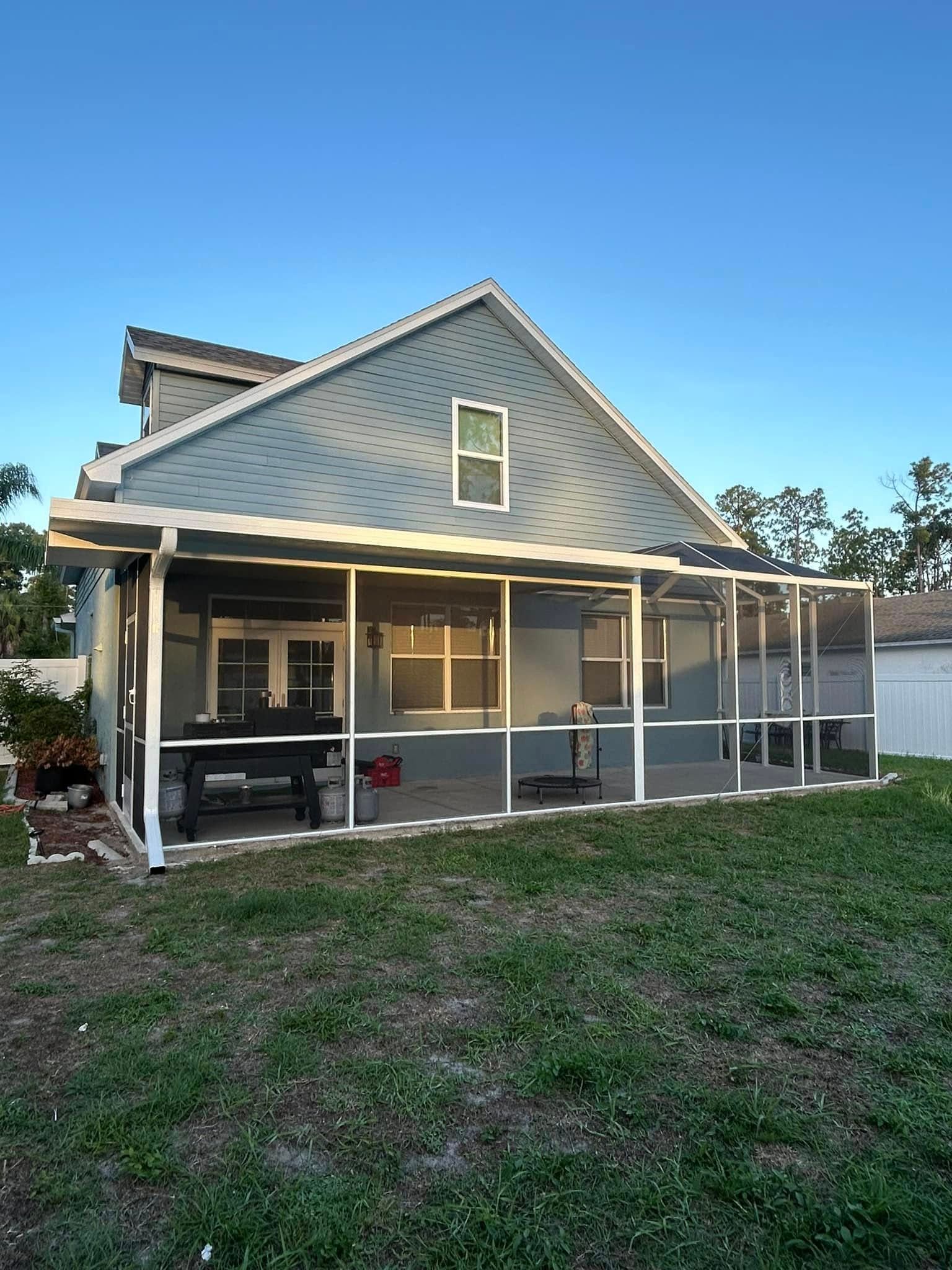 Gray house with screened front porch and white trim, viewed from the yard under a clear blue sky