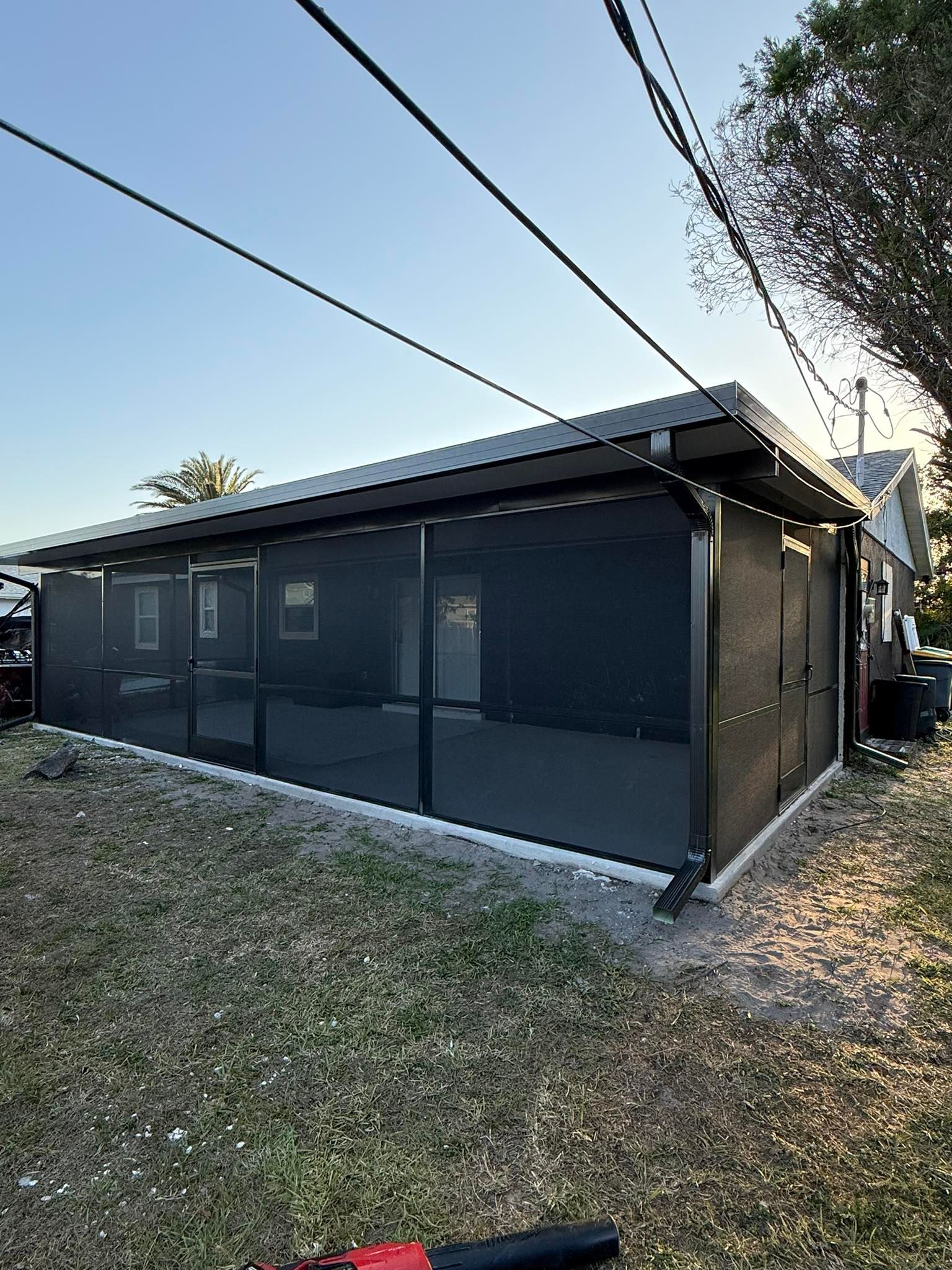 Dark modern house exterior with screened porch, sloped roof, and utility lines overhead.