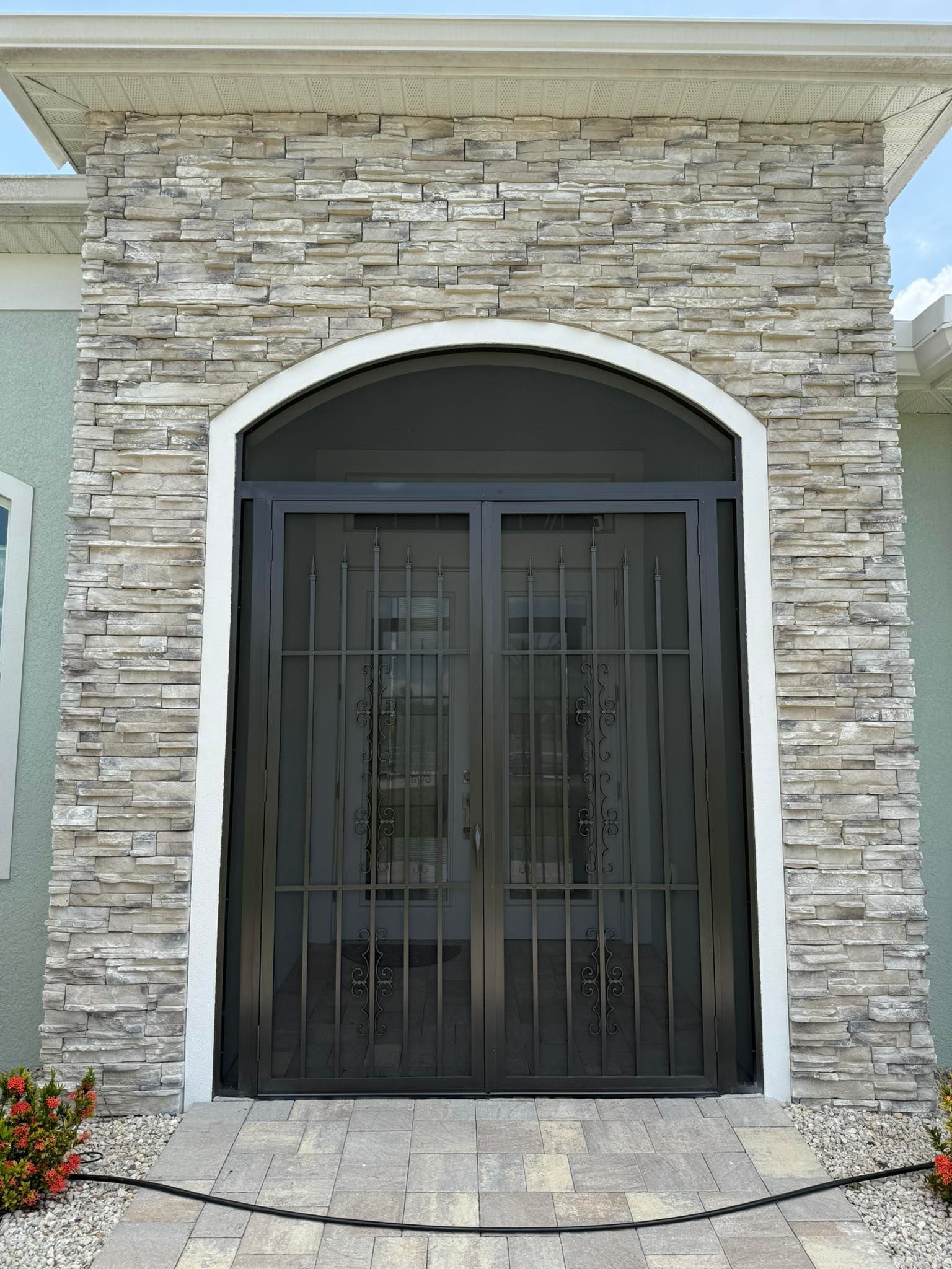 Stone-front entry with black metal double doors and an arched doorway