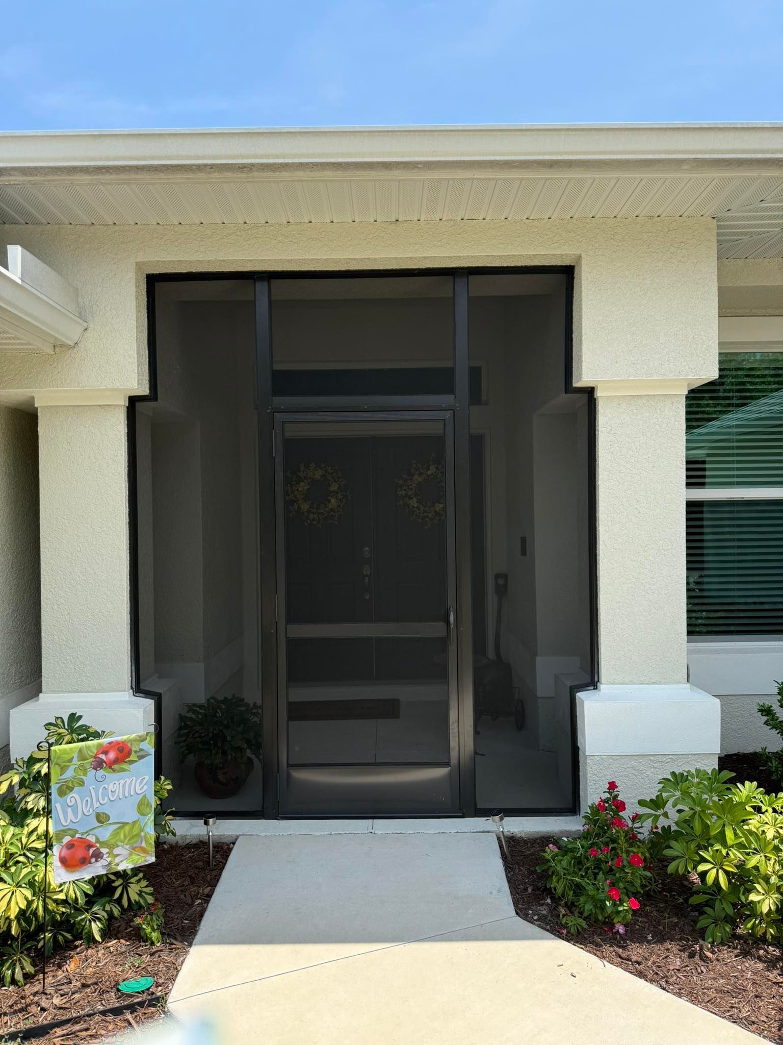 Front entrance with a dark screen door, white stucco walls, and a flower-lined walkway
