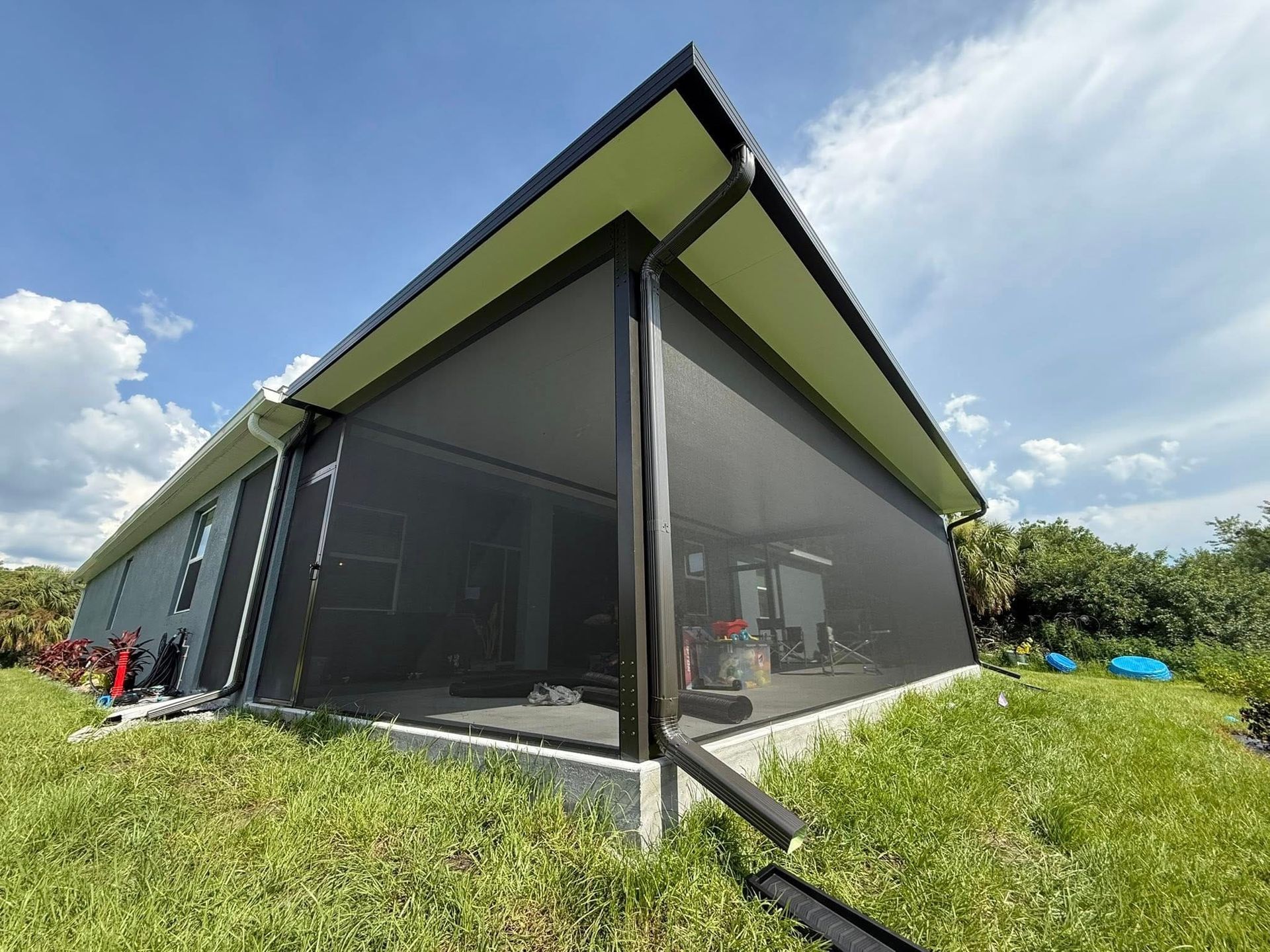 Modern house with dark screened walls and a sloped roof on a grassy hill under a blue sky