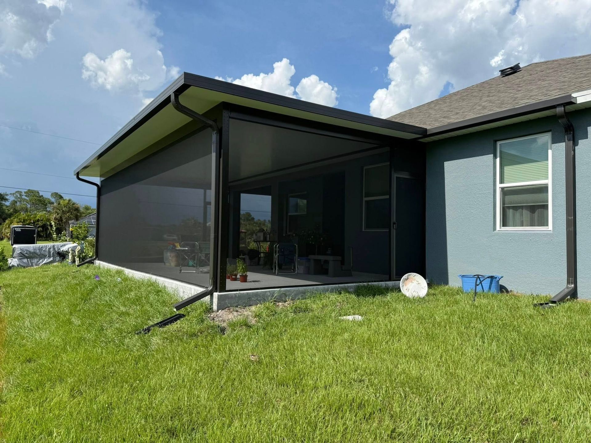 Covered backyard patio attached to a gray house, with screened enclosure and grassy lawn.