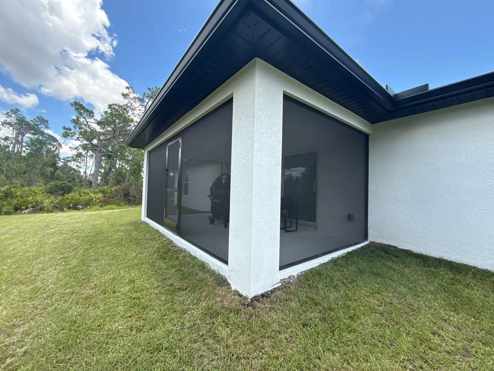 Modern house corner with screened patio, white walls, dark roof, and grassy yard under a blue sky