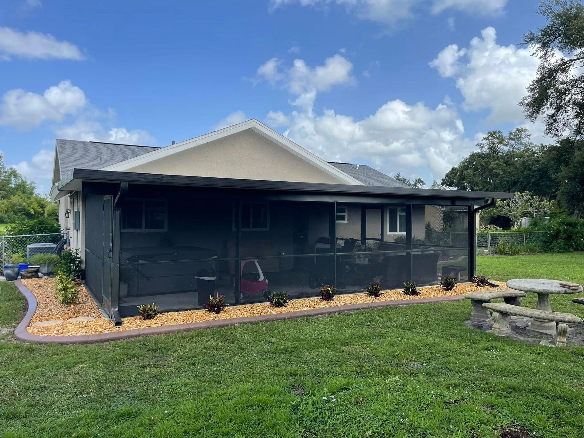 Small black house with screened porch in a grassy yard under a blue sky with clouds