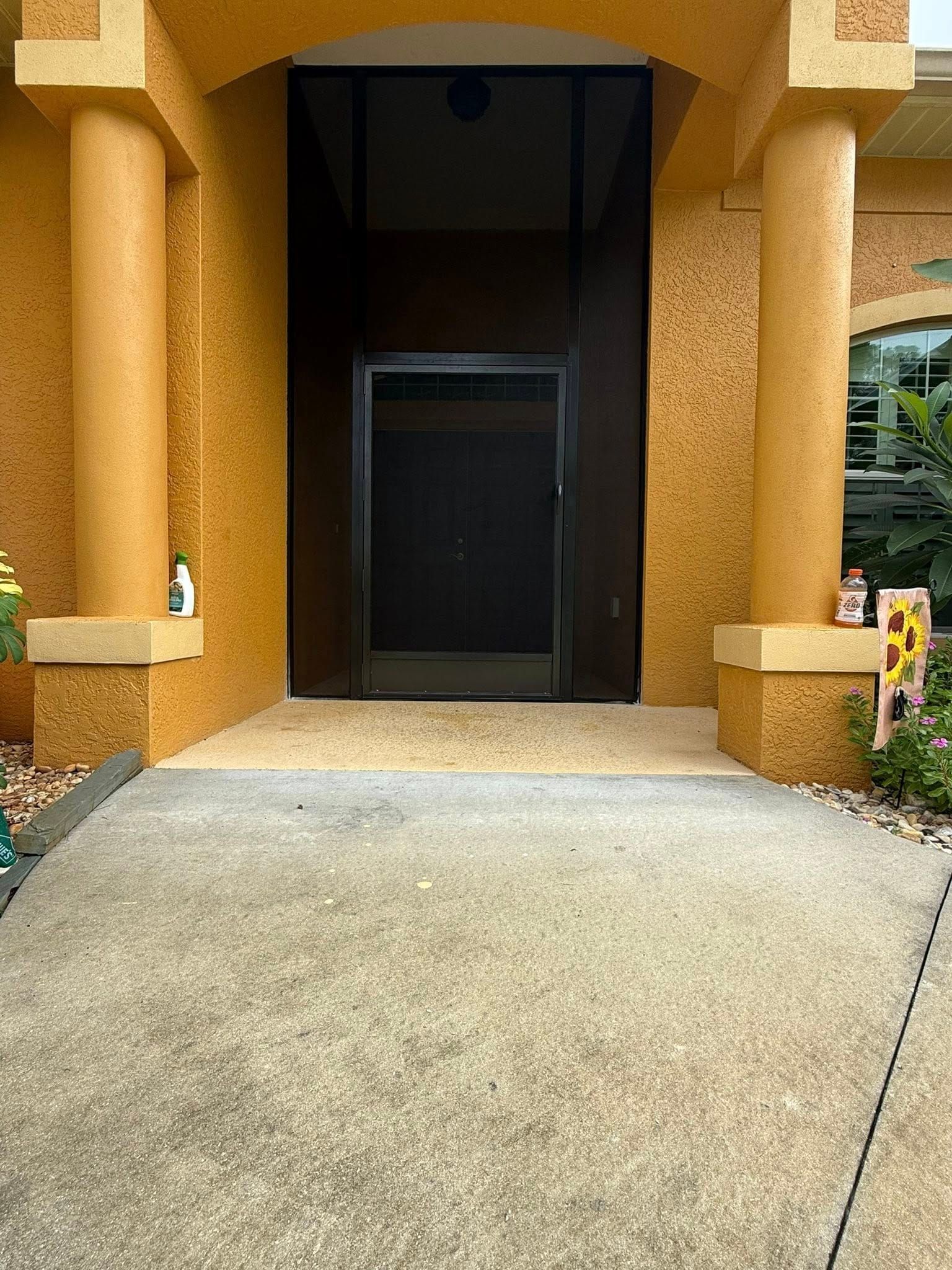 Front entrance with orange columns, dark doorway, and a concrete walkway leading up to it.