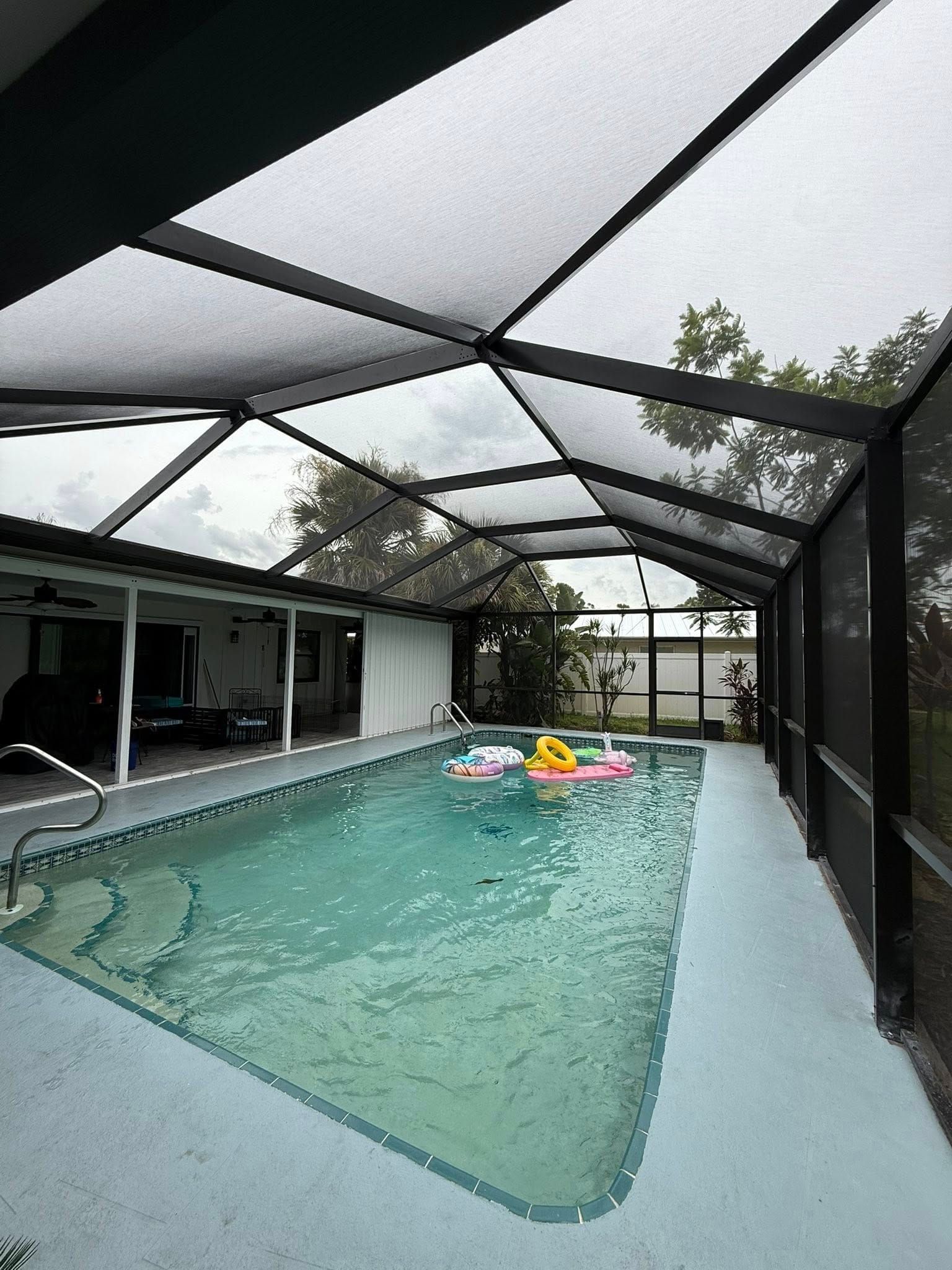 Screened-in backyard pool with clear water and colorful float toys under a covered patio