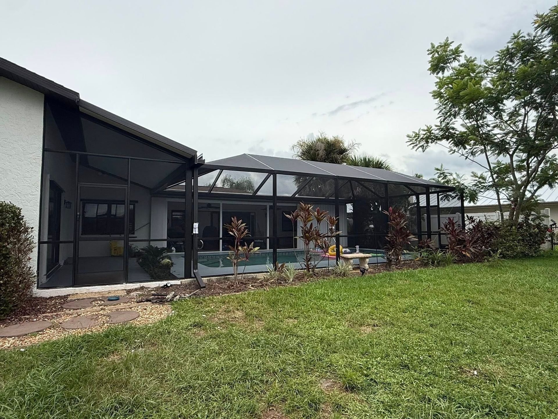 Patio seating beside a modern house, with a black screened enclosure and grassy yard.