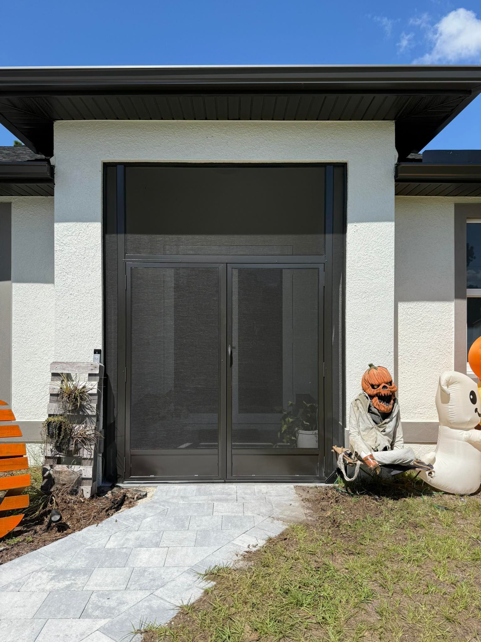 Front entrance with dark sliding glass doors, white stucco walls, stone path, and Halloween decorations.