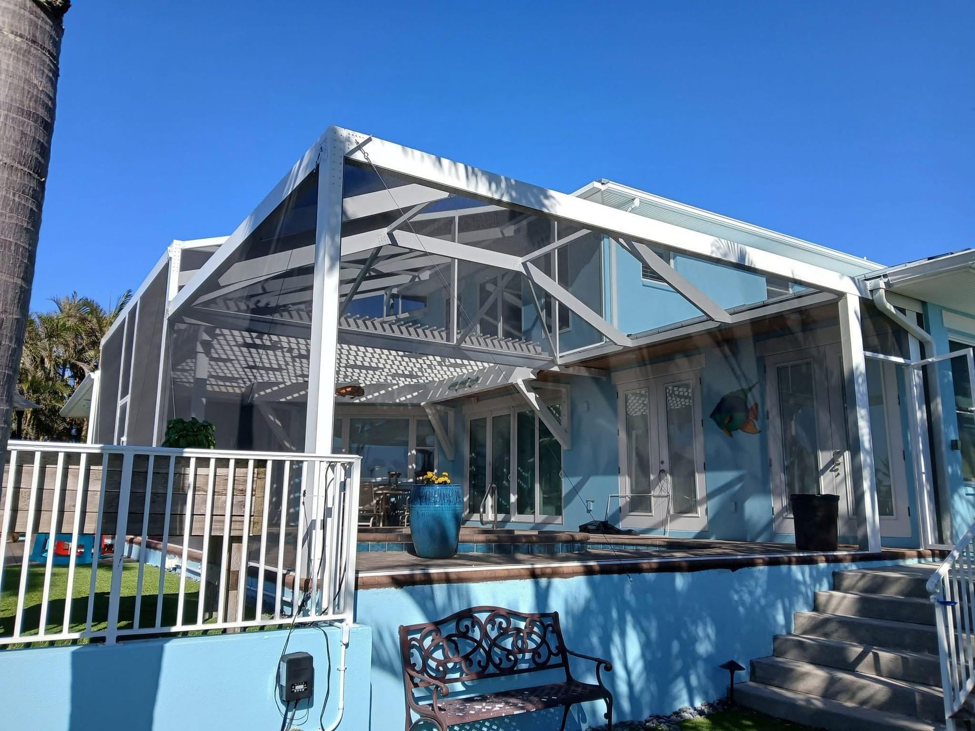 White house with a glass-enclosed porch, blue lower wall, and steps under a clear blue sky
