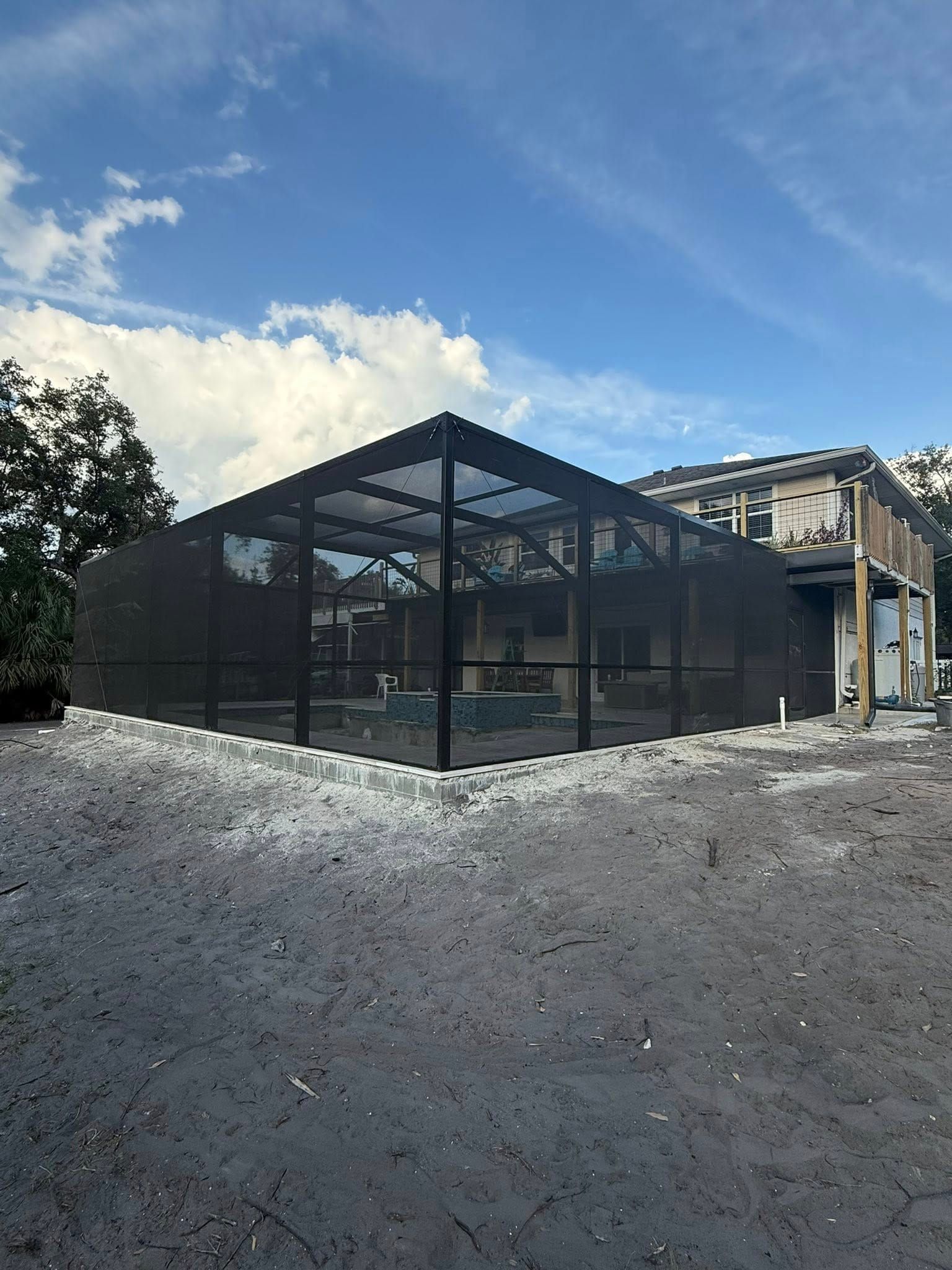 Black mesh enclosure around a building under construction on a gravel lot, beneath a blue sky.