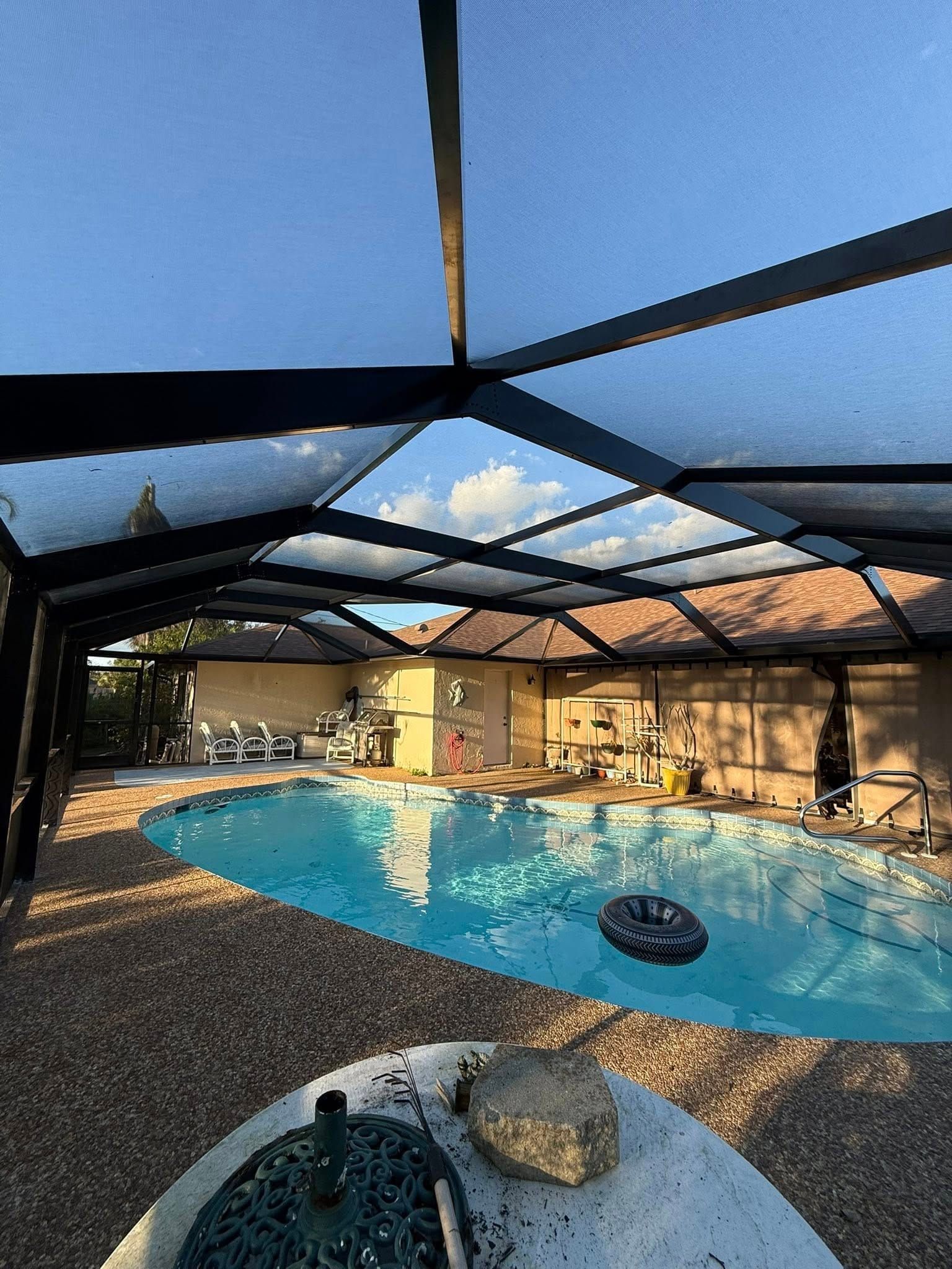 Screened backyard pool with blue water, patio furniture, and a patio roof under a bright sky