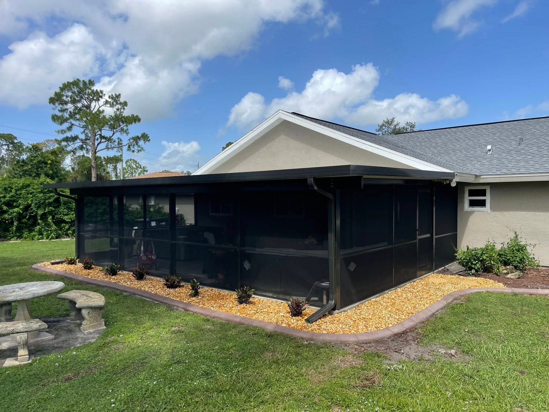 Screened patio enclosure beside a house, with black mesh panels and a stone birdbath in the yard.