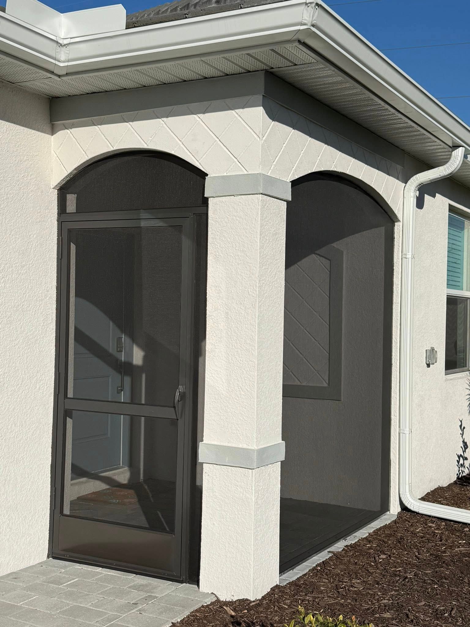 Front porch with arched openings, screened dark door, and white stucco exterior under a tiled roof.