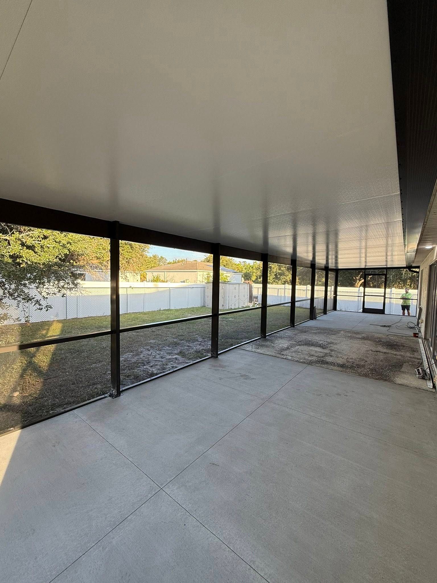 Covered outdoor walkway with white ceiling, black mesh fence, and concrete floor beside a road