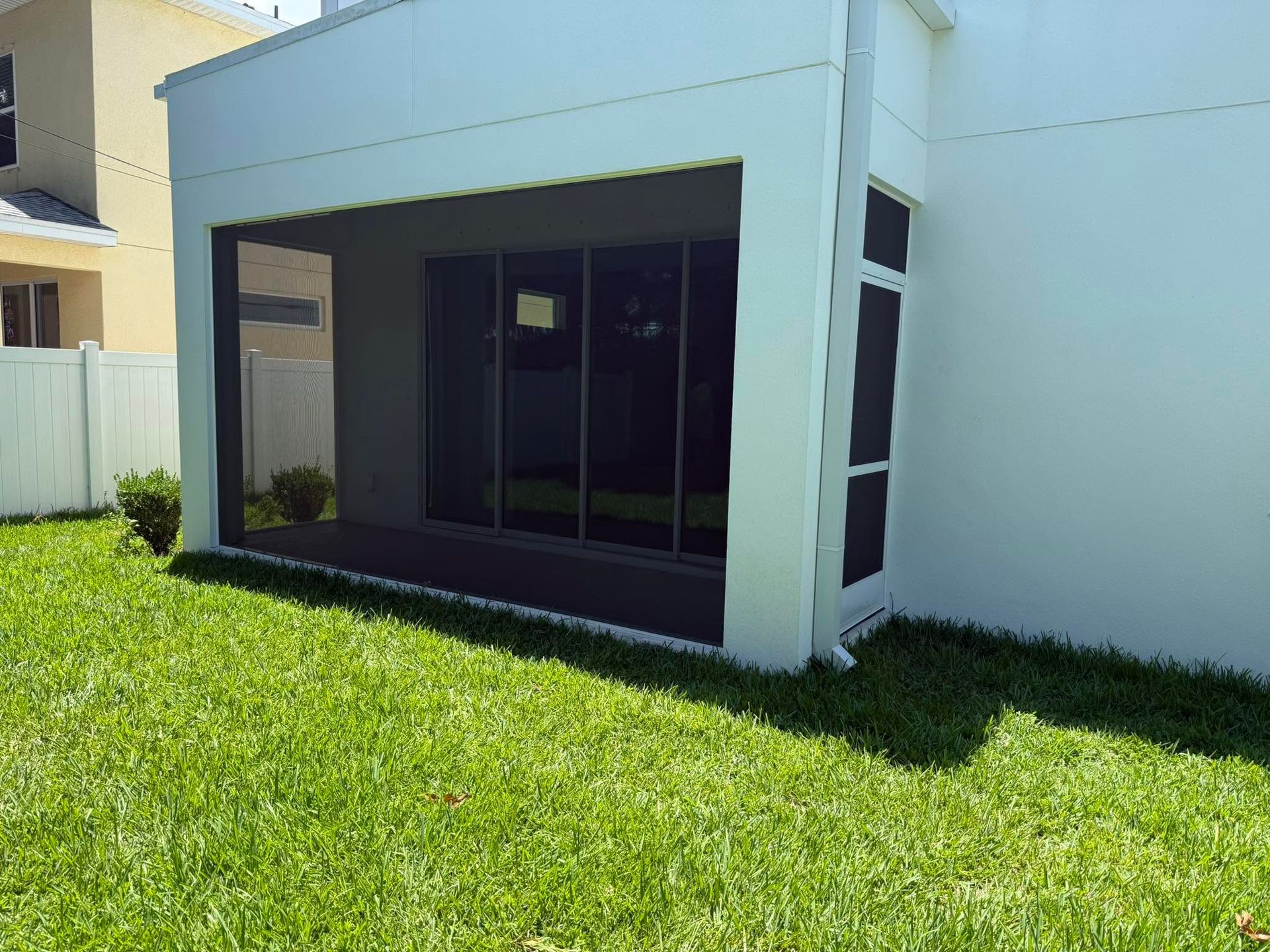 Patio with large dark-framed sliding glass doors beside a white wall and green lawn