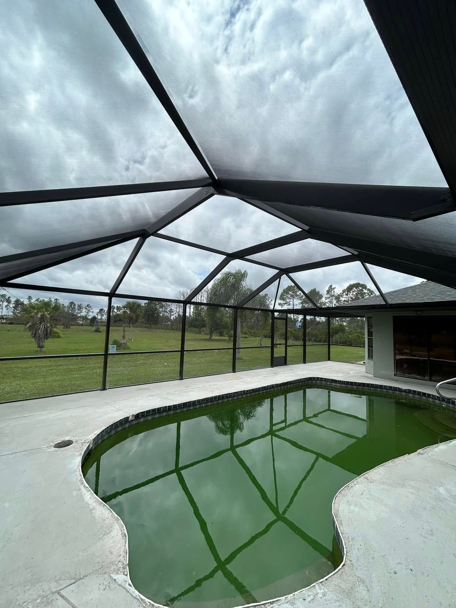 Screened patio with a green pool reflecting a cloudy sky and black roof beams